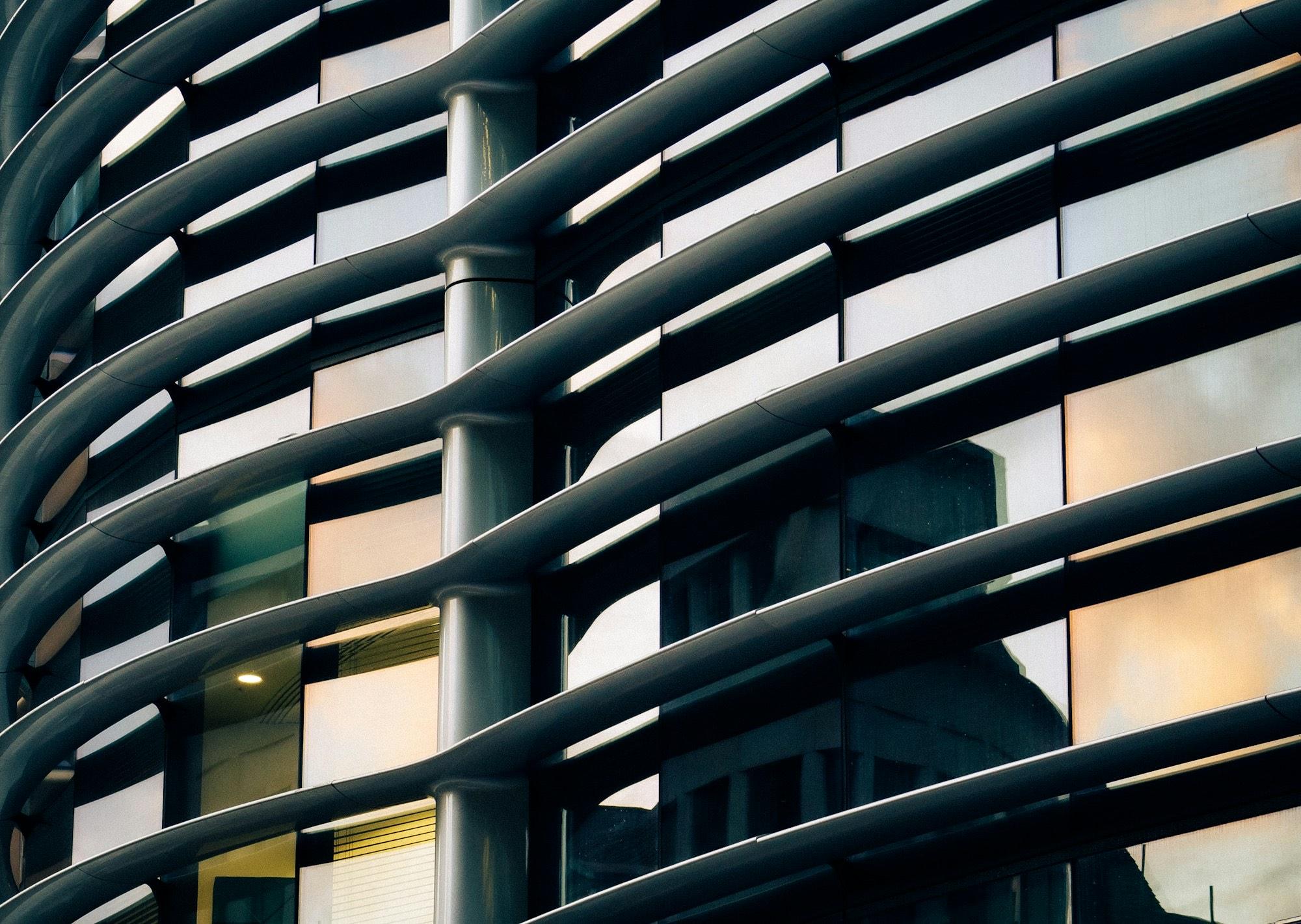 Close-up of a modern glass facade wrapped in sweeping curved metal louvers, warm light showing through some windows.