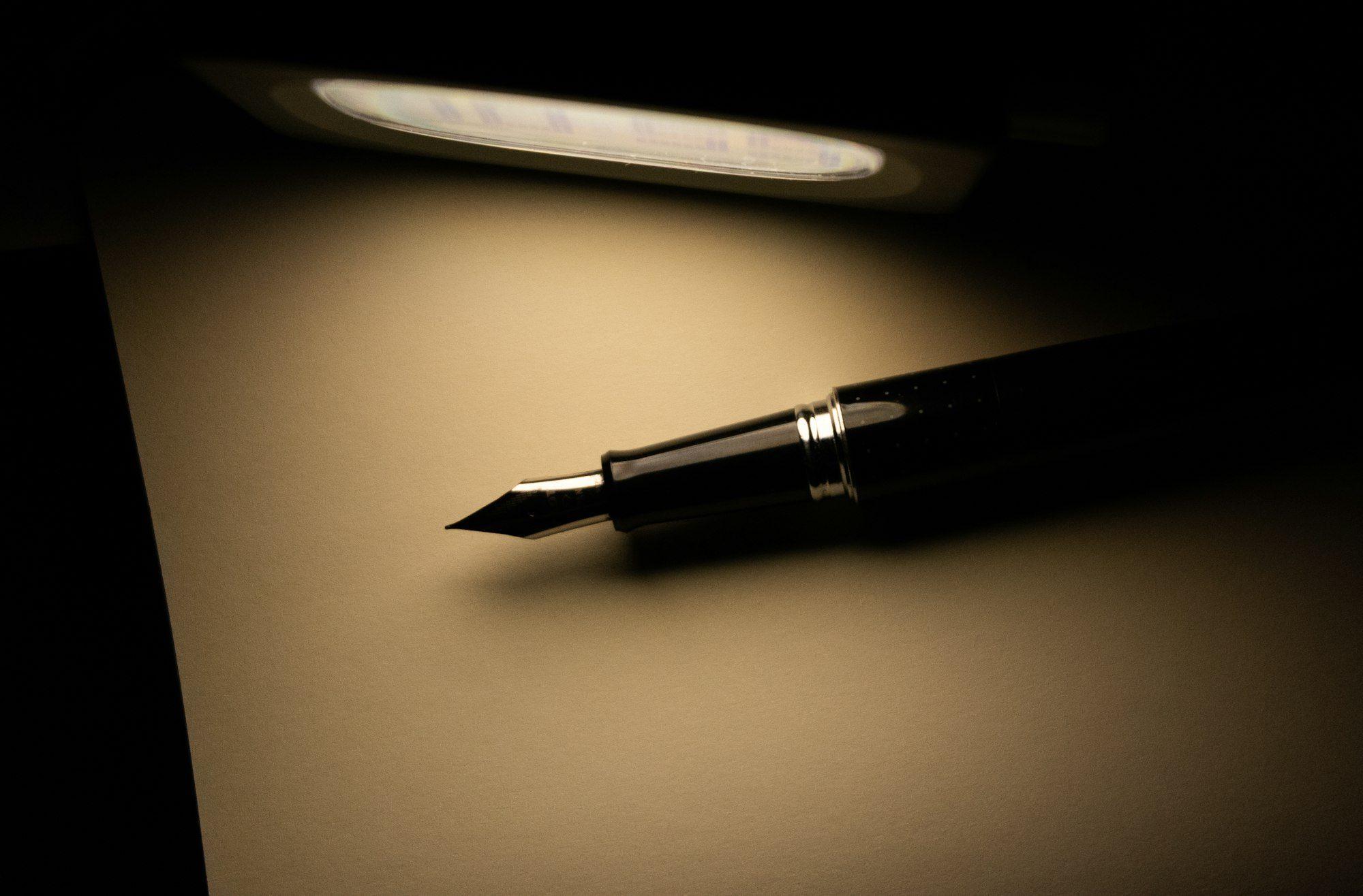A black fountain pen resting on cream paper under the warm glow of a desk lamp.