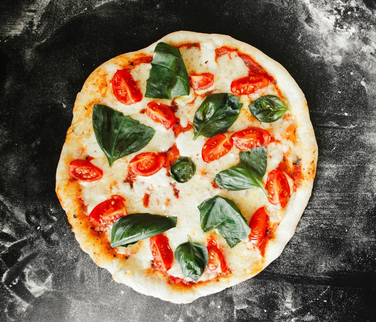 Overhead view of a whole margherita pizza with melted mozzarella, cherry tomatoes and fresh basil.
