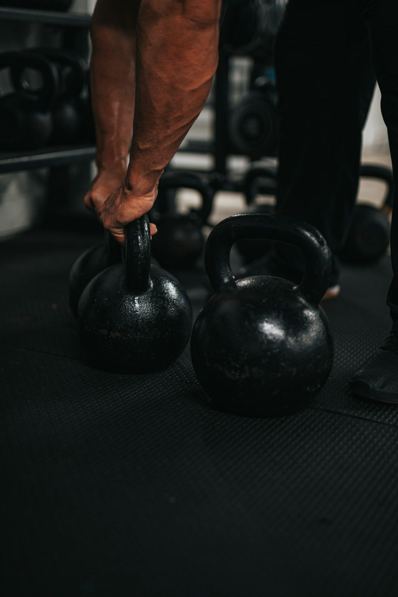 A hand gripping a cast-iron kettlebell on a black gym floor.